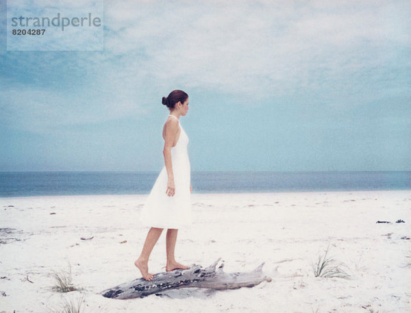 Junge Frau auf Treibholz am Strand stehend  Seitenansicht