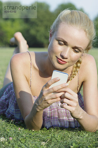 Frau auf Rasen liegend  mit Smartphone