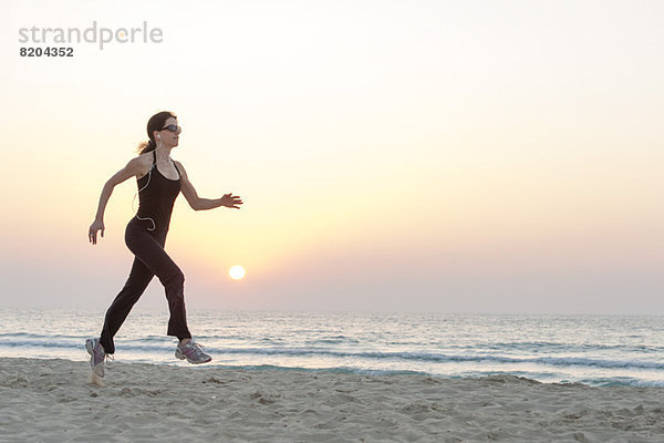 Frau mit Sonnenbrille beim Joggen am Strand bei Sonnenaufgang