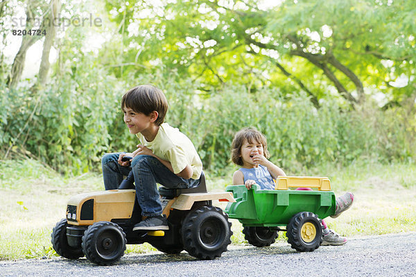 Junge Geschwister fahren auf Spielzeugtraktor