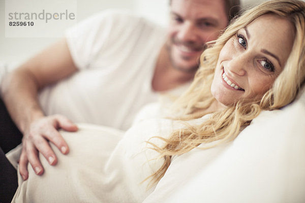 Porträt einer glücklichen schwangeren Frau mit einem im Bett liegenden Mann