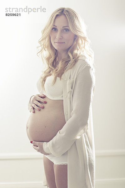 Porträt einer schwangeren Frau  die den Bauch zu Hause hält.