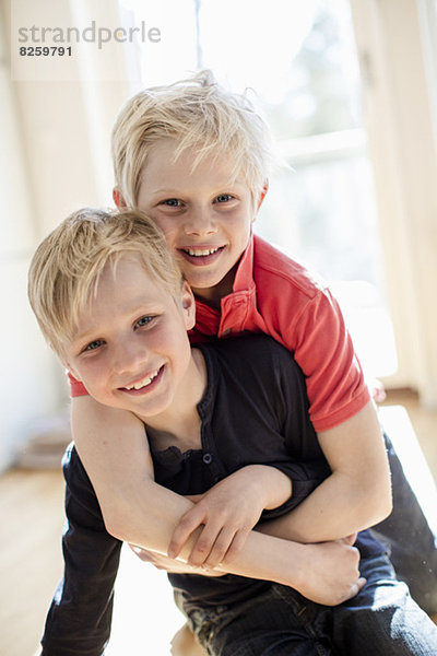 Porträt eines Jungen  der den Bruder von hinten im Haus umarmt.