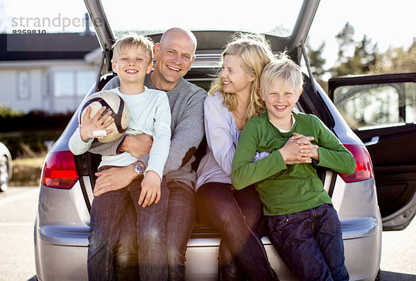 Porträt einer glücklichen Familie  die auf dem Kofferraum sitzt.