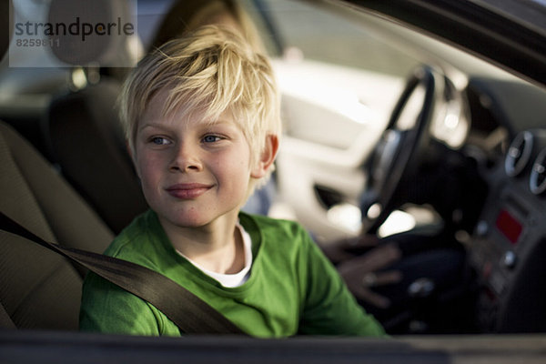 Lächelnder kleiner Junge  der durch das Autofenster schaut.