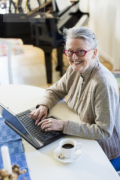 Hochwinkel-Porträt einer glücklichen Seniorin mit Laptop am Tisch