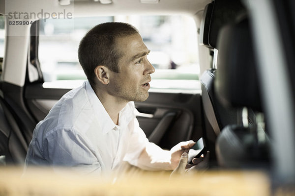 Seitenansicht eines Geschäftsmannes mit Mobiltelefon im Taxi