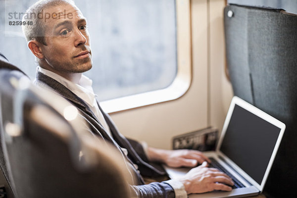 Der reife Geschäftsmann schaut weg  während er den Laptop im Zug benutzt.