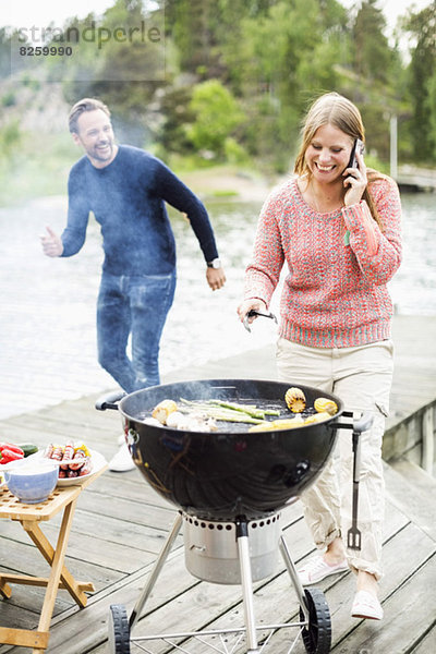 Fröhliche Frau beim Grillen mit dem Mann am Pier