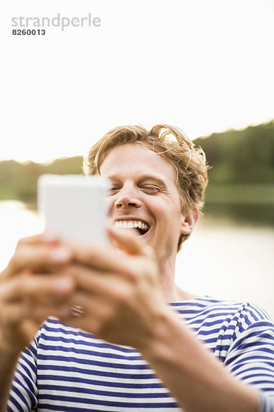 Mann lacht beim Lesen von Textnachrichten auf dem Handy im Freien
