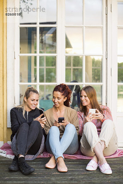 Freundinnen nutzen Mobiltelefone im Sommerhaus