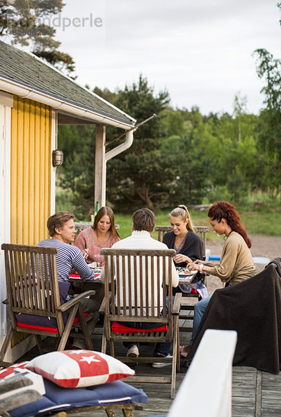 Gruppe von Freunden sitzt am Esstisch vor dem Sommerhaus