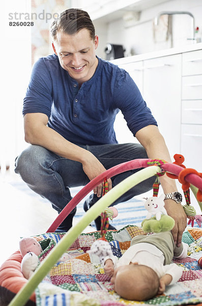 Glücklicher Vater schaut Baby auf Spielmatte in der Küche liegend an