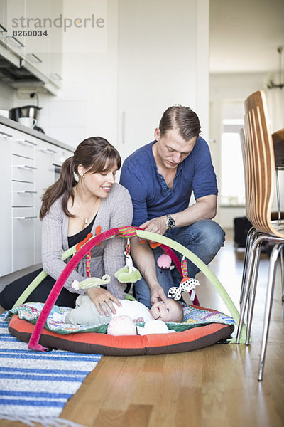 Eltern streicheln Baby Mädchen liegend in Spielmatte in der Küche