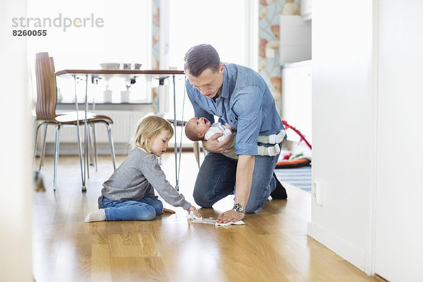 Vater putzt den Boden mit der Tochter und hält das Mädchen zu Hause.