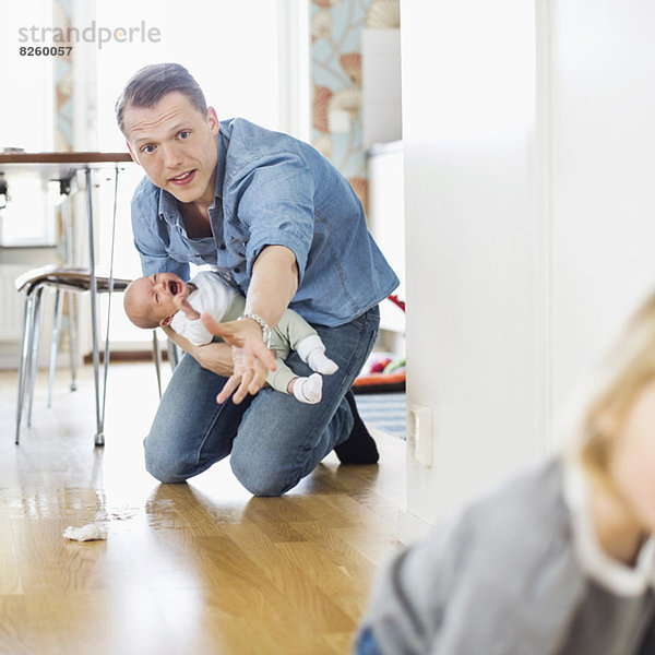 Vater hält weinendes Baby  während er die Tochter zu Hause auf dem Boden hält.