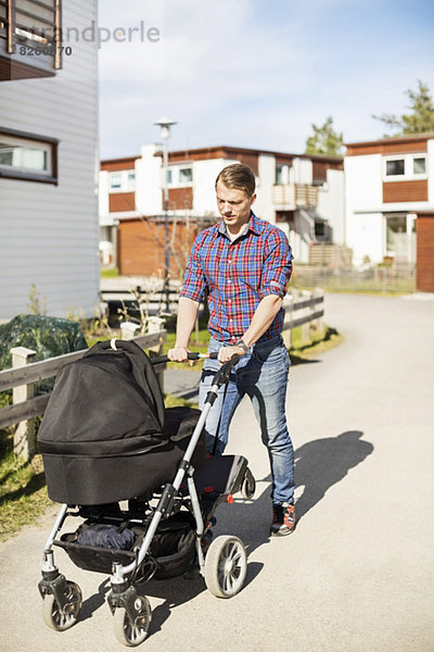 Mittelgroßer Mann mit Kinderwagen auf sonniger Straße