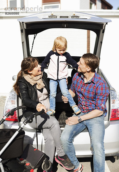 Zufriedene Eltern mit Tochter und Kinderwagen im Kofferraum