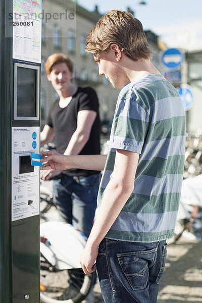 Junger Mann bezahlt mit Kreditkarte beim Fahrrad-Sharing-System