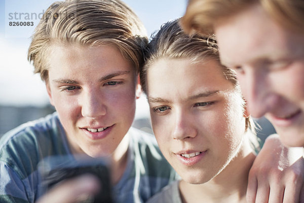 Männliche Freunde beim gemeinsamen Lesen von Textnachrichten auf dem Handy im Freien