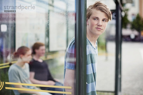 Junger Mann wartet mit Freunden an der Bushaltestelle