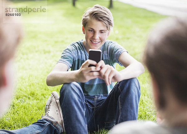 Glücklicher junger Mann beim Fotografieren von Freunden im Park