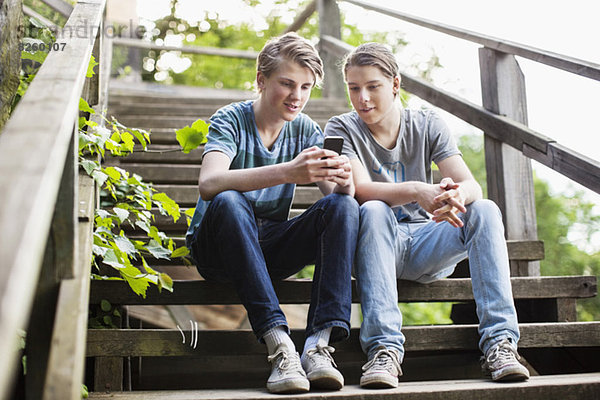 Junge männliche Freunde mit dem Handy auf der Treppe im Freien