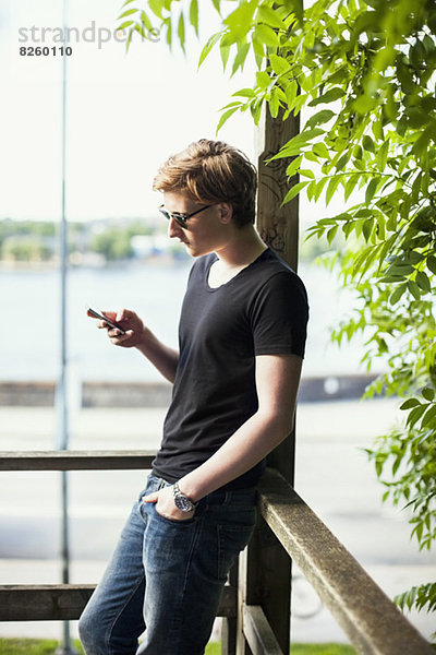 Junger Mann mit Handy auf dem Balkon