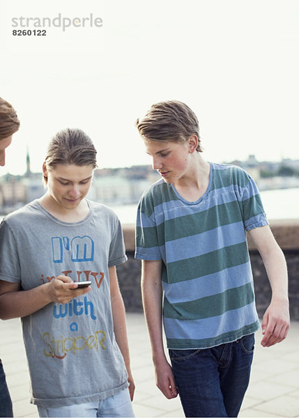 Junge Männer  die beim Gehen auf dem Bürgersteig gemeinsam mit dem Handy telefonieren
