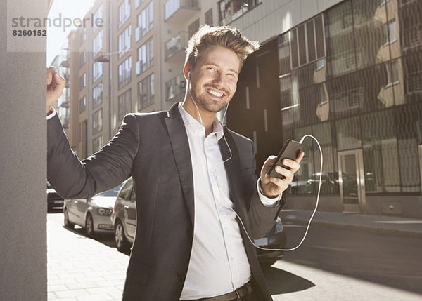 Glücklicher junger Geschäftsmann  der Musik über das Handy auf der Straße hört.
