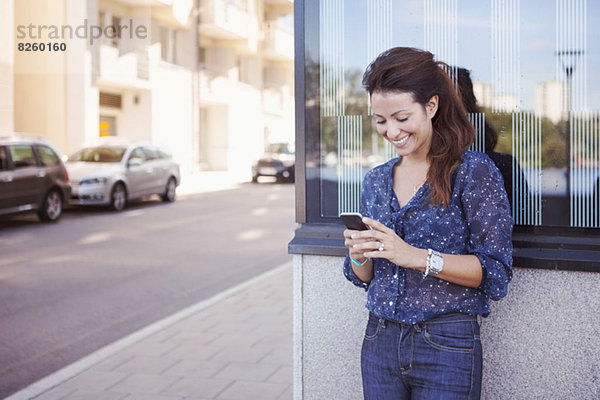 Glückliche Geschäftsfrau mit Handy an der Wand auf dem Bürgersteig