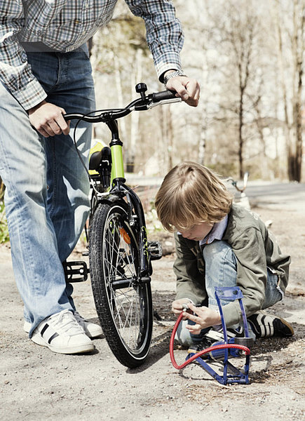 Junge füllt Fahrradreifen mit Fußpumpe während Vater auf der Straße steht