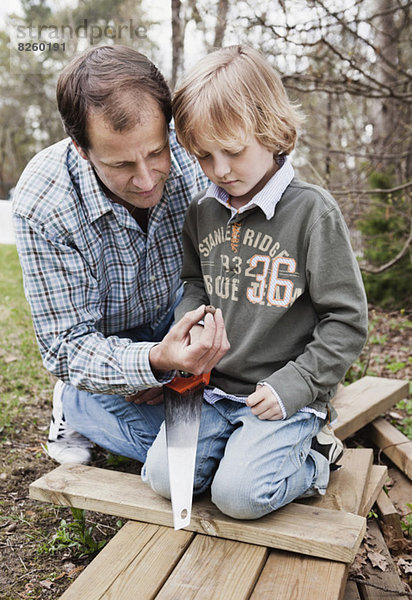 Zwei Generationen Rüden mit Säge und Holzbohlen im Hof