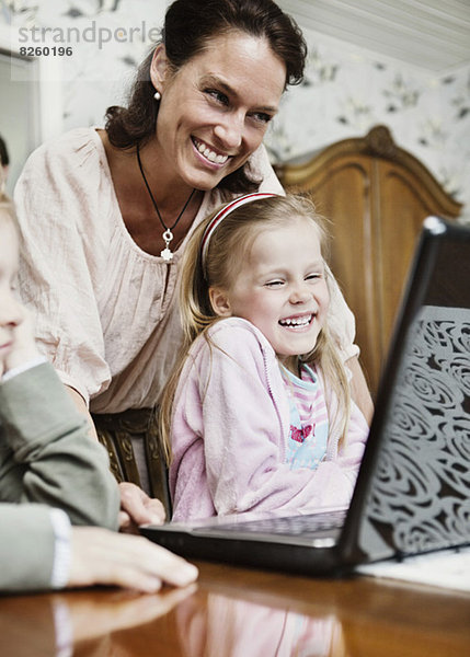Glückliche Mutter und Kinder beim Betrachten des Laptops im Haus