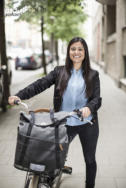 Porträt einer fröhlichen Geschäftsfrau mit Fahrrad auf dem Bürgersteig