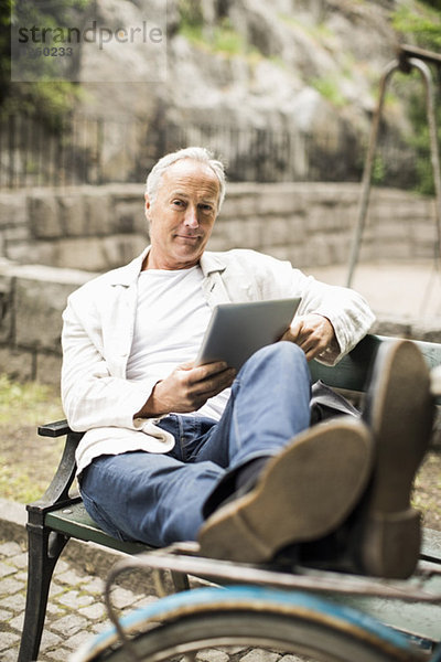 Porträt eines Geschäftsmannes mit Füßen oben auf dem Fahrrad mit digitalem Tablett im Park