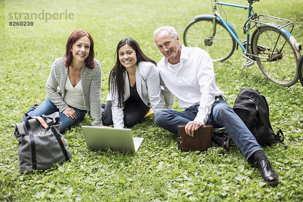 Portrait von Geschäftsleuten mit Laptop auf Rasen im Park