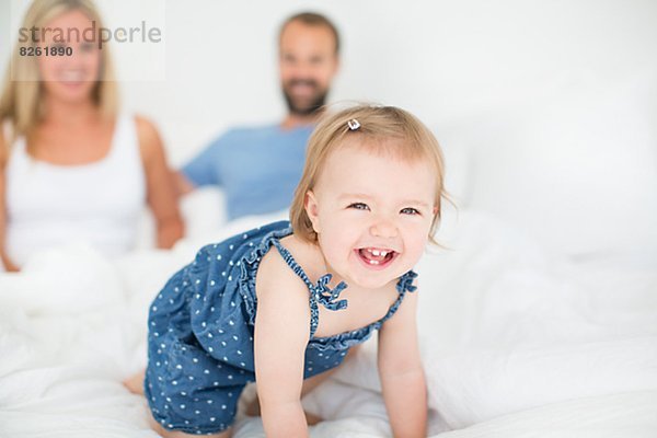 Little girl crawling on bed  mother and father in background