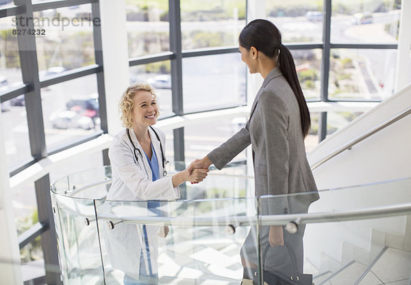 Arzt und Geschäftsfrau beim Händeschütteln auf der Treppe im Krankenhaus