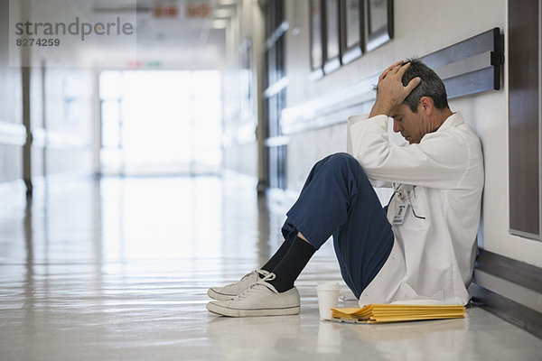 Arzt sitzt auf dem Boden im Flur des Krankenhauses mit Kopf in den Händen