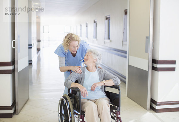 Krankenschwester mit alternder Patientin im Rollstuhl im Krankenhausflur