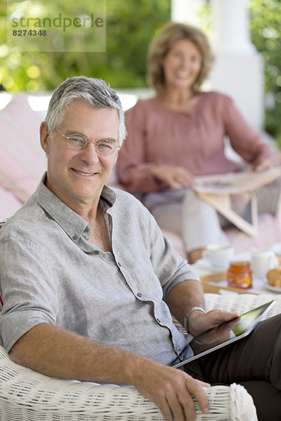 Senior Mann mit digitalem Tablett im Sessel auf der Terrasse