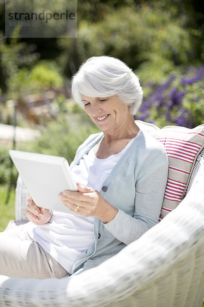 Seniorin mit digitalem Tablett im Sessel