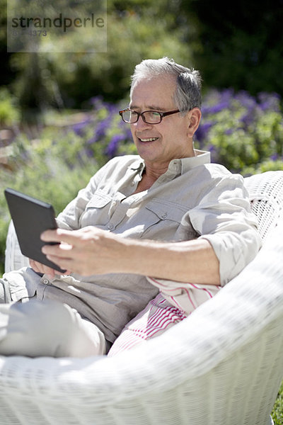 Senior Mann mit digitalem Tablett im Sessel