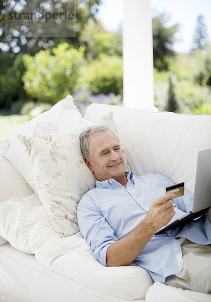 Senior Mann online einkaufen auf der Terrasse Sofa