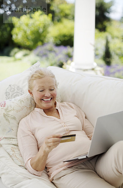 Seniorenfrau beim Online-Shopping auf dem Terrassensofa