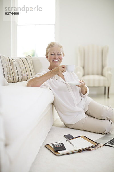 Seniorin trinkt Kaffee auf dem Wohnzimmerboden
