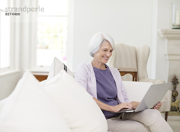 Seniorin mit Laptop auf Sofa im Wohnzimmer