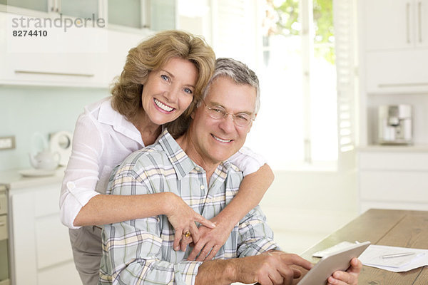 Porträt eines lächelnden Seniorenpaares mit digitalem Tablett in der Küche