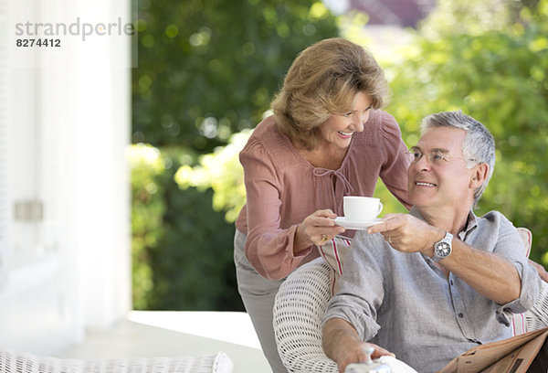 Seniorenfrau bringt Mann eine Tasse Kaffee auf die Terrasse